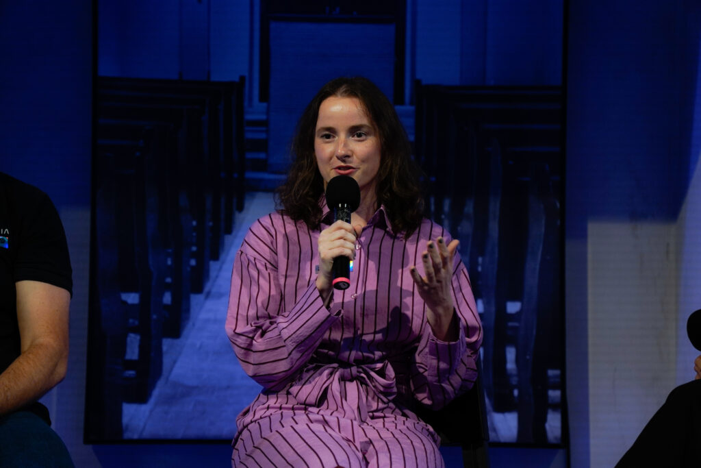 Laura Ďorďová z Tapaye sedí s mikrofónom na modro nasvietenom pódiu Startup Awards Slovensko a gestikuluje počas panelovej diskusie.
