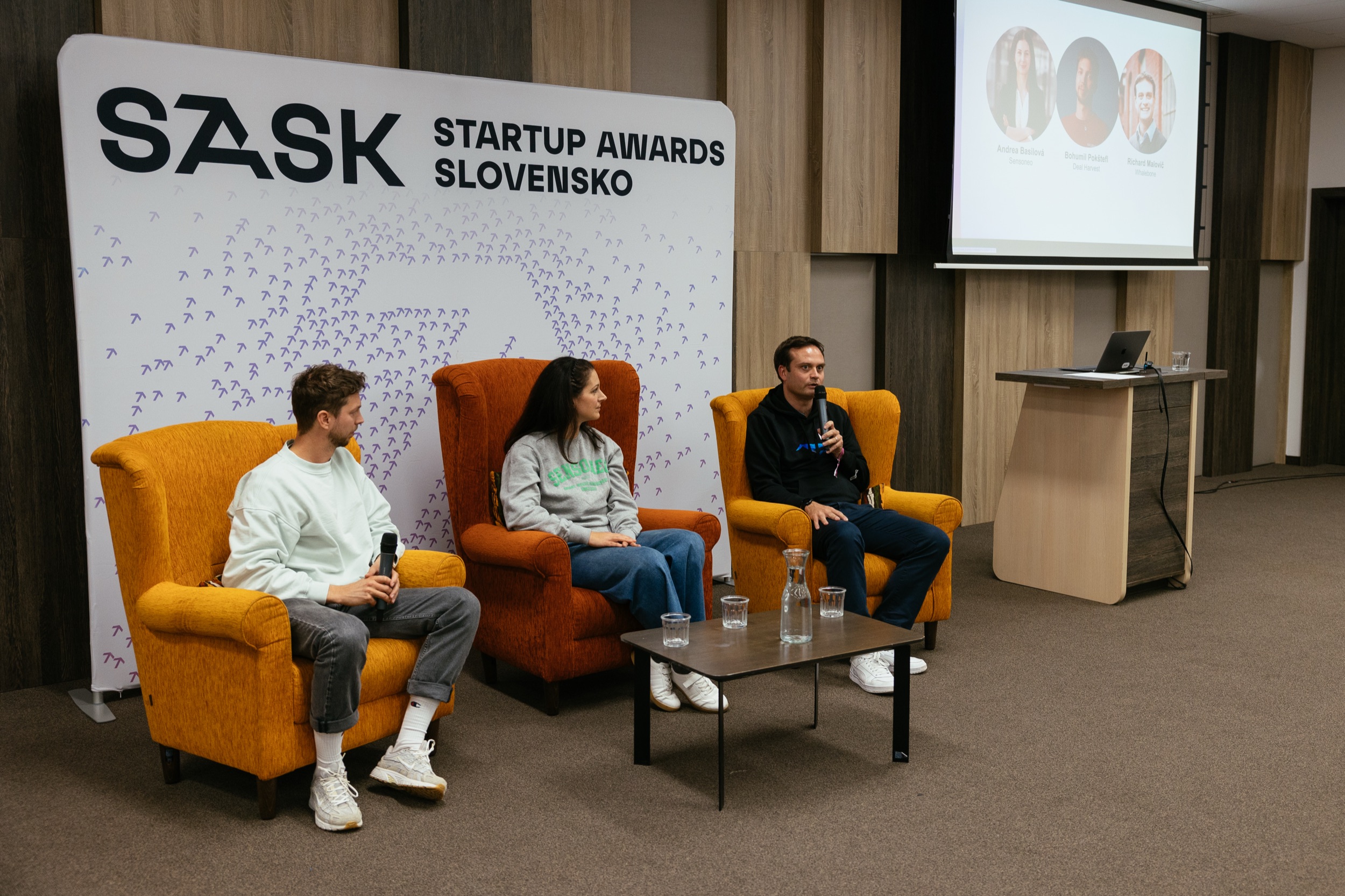 Diskusia troch hostí v kreslách pred stenou Startup Awards Slovensko